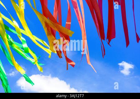 Nastri di plastica verdi, gialli, arancioni e rossi che soffiano nel vento contro un cielo blu. Foto Stock