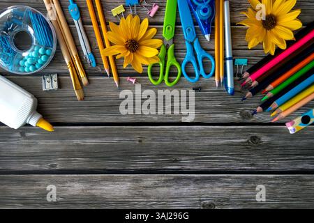 Forniture scolastiche colorate e girasoli su sfondo in legno. Una vivace collezione di forniture scolastiche, tra cui matite, forbici, matite colorate Foto Stock