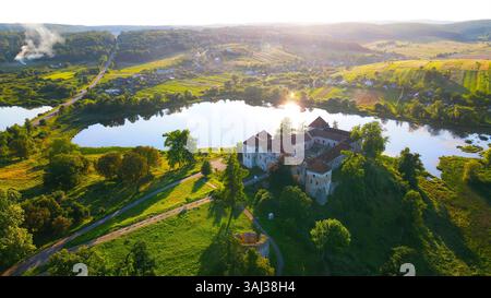 Vista aerea di un castello vicino a un fiume circondato da campi verdi. Una vista aerea mozzafiato di un castello storico annidato da un fiume calmo, circondato da Foto Stock