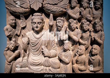 WASHINGTON DC - Un pannello di rilievo scisto dell'antica Gandhara (moderno Pakistan/Afghanistan) che raffigura il Buddha che esegue il suo primo sermone, esposto allo Smithsonian National Museum of Asian Art Creato durante la dinastia Kushan (fine II-inizio III secolo d.C.), questo pannello faceva parte di una serie di quattro scene che adornavano uno stupa buddista. La scultura mostra il Buddha con la mano sollevata in un gesto rassicurante, circondato da discepoli attenti che si distinguono per il loro aspetto: Seguaci laici che indossano gioielli e monaci dalla testa rasata senza ornamenti. Foto Stock