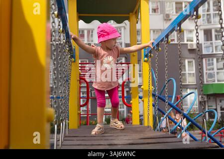Un bambino piccolo in un cappello a secchio gioca nel parco giochi vicino alla casa. Persone Foto Stock