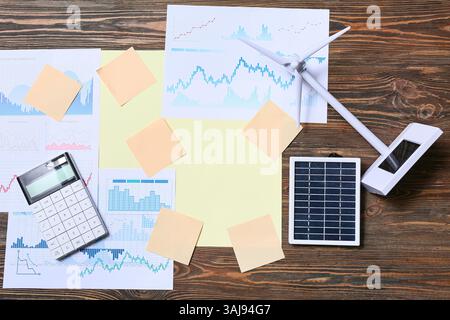 Diagrammi con note adesive vuote e modello di turbina eolica su sfondo in legno. Concetto di energia verde Foto Stock