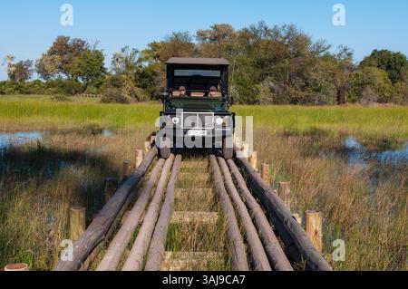 Un veicolo da safari che attraversa un ponte di tronchi, Botswana, Delta dell'Okavango, Abu Camp Foto Stock