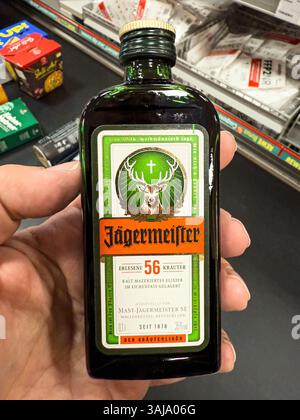 Mano che tiene in mano una piccola bottiglia di digestione jagermeister in un supermercato, pronta per essere acquistata - FRANCOFORTE, GERMANIA - 9 APRILE 2025 Foto Stock