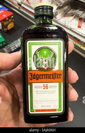 Tenere a mano una piccola bottiglia di liquore jagermeister in un supermercato, che mostra l'iconico digestivo tedesco - FRANCOFORTE, GERMANIA - 9 APRILE 2025 Foto Stock