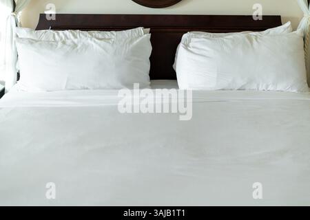 Una spaziosa camera da letto presenta un grande letto adornato con fresche lenzuola bianche e soffici cuscini, creando un'atmosfera invitante e confortevole per rilassarsi Foto Stock