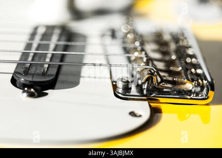 La chitarra elettrica gialla mette in risalto il ponte cromato lucido e le corde tese contro un picchetto bianco. Sfondo sfocato con luci bokeh Foto Stock