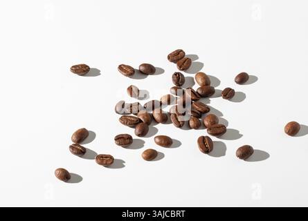 Chicchi di caffè arrosto sparsi su uno sfondo bianco Foto Stock