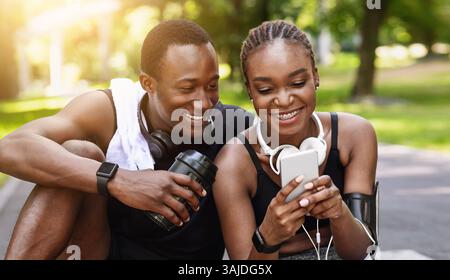 Montare la coppia nera utilizzando lo smartphone dopo l'allenamento all'aperto, controllando le misurazioni dell'attività fisica Foto Stock