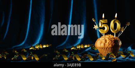 Numero 50 di candele per festeggiare l'oro e piccole stelle in dolce cupcake su sfondo blu brillante in velluto. Concetto di celebrare il compleanno, l'anniversario Foto Stock