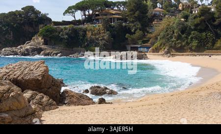 Splendida insenatura di Cala Sant Francesc a Blanes, con sabbia dorata, acque turchesi cristalline, affioramenti rocciosi e case incastonate sulle scogliere. Foto Stock