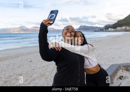 Sorelle che si abbracciano e si fanno un selfie in spiaggia Foto Stock