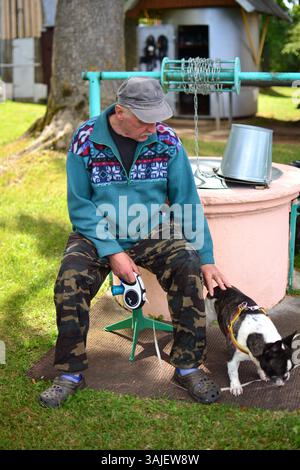 Un uomo anziano seduto accanto al vecchio pozzo d'acqua e toccando bulldog francesi nel villaggio. Uomo anziano che passa del tempo in campagna andando a camminare con il suo cane. Foto Stock