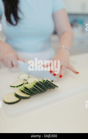 Donna che affetta zucchine su un tagliere bianco in cucina. Foto Stock