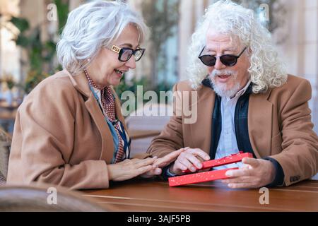 Felice coppia senior caucasica che si scambia un regalo in un caffè all'aperto momento gioioso Foto Stock