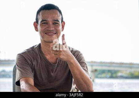 Giovane uomo vietnamita felice su una barca turistica che porta i turisti sul fiume a Hoi An Vietnam. Giovane uomo asiatico lavoratore sorridente e dare colpi su. Viaggiare Foto Stock