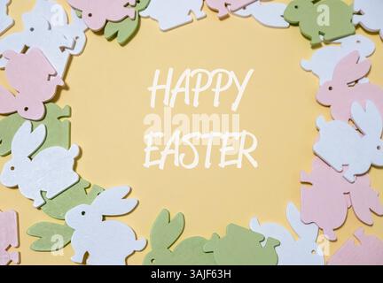 Colorata corona coniglietto pasquale con un messaggio pasquale bianco e rosa. La corona è fatta di piccoli conigli colorati ed è circondata da un dorso giallo Foto Stock