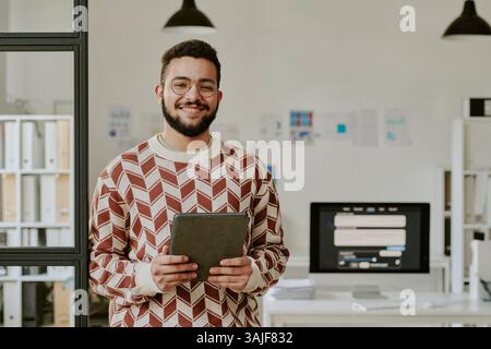 Ritratto in vita di un bellissimo programmatore giovane adulto con tavoletta nera che sorride ampiamente per la foto Foto Stock