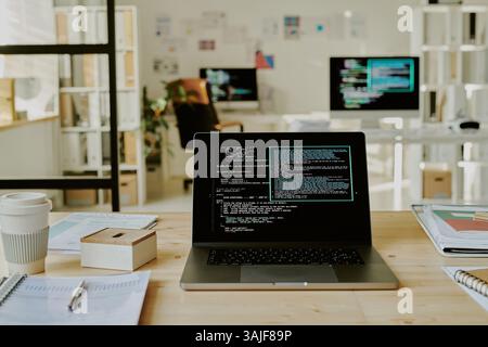 Primo piano medio di un computer portatile con codici sullo schermo sopra un tavolo di legno in ufficio Foto Stock