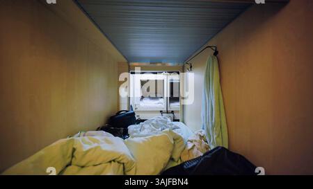 Camera d'albergo con capsula disordinata con letto e asciugamano appesi Foto Stock