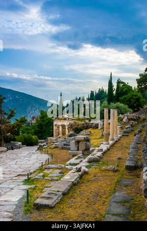Percorso principale con colonne erette e Tesoro di Atene nel sito archeologico di Delfi, Grecia centrale Foto Stock
