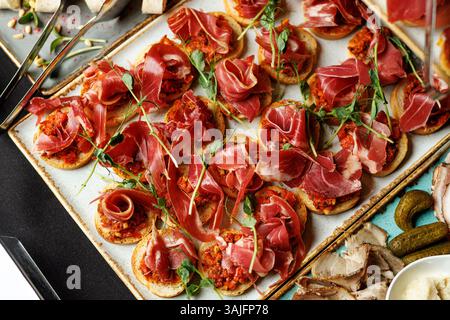 Vista dall'alto di un piatto rustico con tapas assortite ricoperte da prosciutto a fette sottili, guarnito con erbe aromatiche Foto Stock