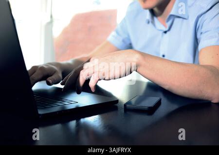 un uomo d'affari lavora online su un laptop, uno smartphone si trova nelle vicinanze, un programmatore elabora una grande quantità di dati Foto Stock