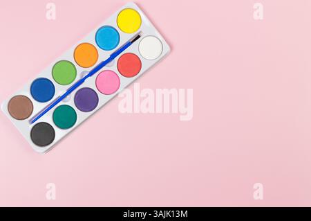 Vista dall'alto dell'acquerello e del pennello su sfondo rosa. Pittura, arte, spazio copia, piatto. Foto Stock