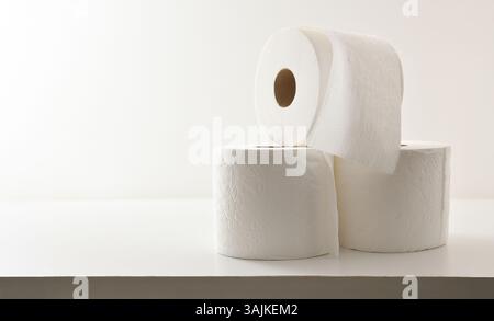 Tre rotoli di carta igienica impilati con consistenza su tavolo in legno bianco e sfondo bianco isolato. Vista frontale. Foto Stock