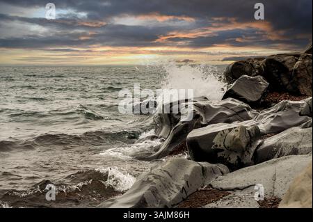Costa rocciosa al tramonto con onde che si infrangono contro la costa Foto Stock
