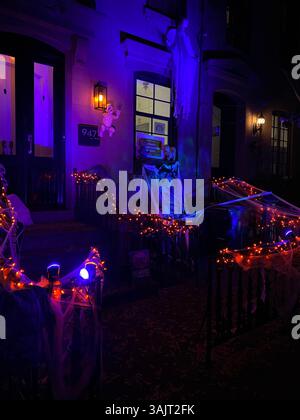 Casa di Halloween di notte con luci arancioni e viola accese, spettrale scheletro sul portico, zucche intagliate sui gradini, decorazioni fantasma appese Foto Stock