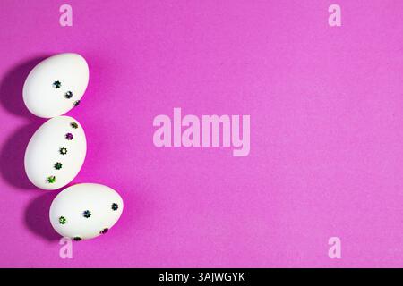 Uova di Pasqua fatte a mano su sfondo viola per un arredamento primaverile. Uova di Pasqua creative decorate con gemme floreali e quadrate poste ordinatamente su un dorso viola Foto Stock