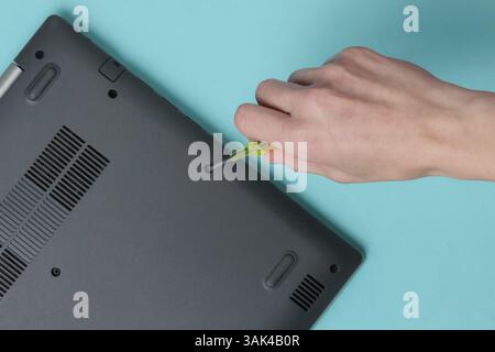 Centro di assistenza. Riparazione di notebook. Il cacciavite a mano femmina svita i bulloni del computer portatile su sfondo blu Foto Stock