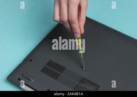Centro di assistenza. Riparazione di notebook. Il cacciavite a mano femmina svita i bulloni del computer portatile su sfondo blu Foto Stock