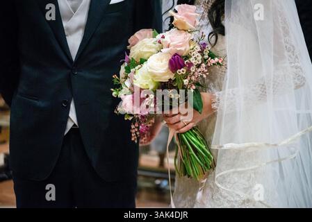 Vista ravvicinata di una sposa che tiene un bellissimo bouquet durante una cerimonia nuziale. La coppia sta insieme con un'atmosfera gioiosa. Foto Stock