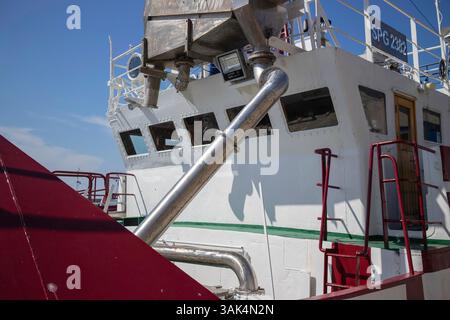 Una grande barca con uno scafo rosso e bianco e un tubo d'argento che esce dal lato. Il tubo è fissato a un grande contenitore Foto Stock