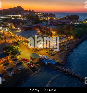 Vista aerea di un resort sulla spiaggia al tramonto, con pedalò, sedie a sdraio e illuminazione calda. Foto Stock