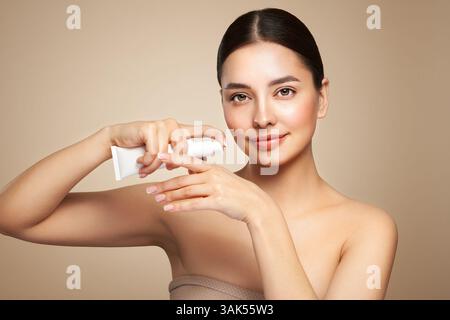 Bella donna con una bottiglia di crema idratante. Video di una donna dalla pelle perfetta su sfondo beige. Concetto di bellezza e cura della pelle Foto Stock