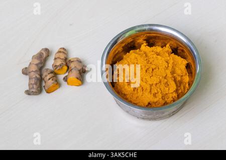 Pasta di curcuma grezza in un recipiente di acciaio su una superficie di legno chiaro. Foto Stock
