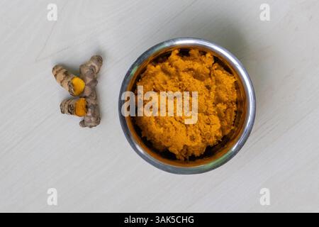 Vista dall'alto della pasta di curcuma grezza in una ciotola di acciaio su uno sfondo di legno chiaro. Foto Stock