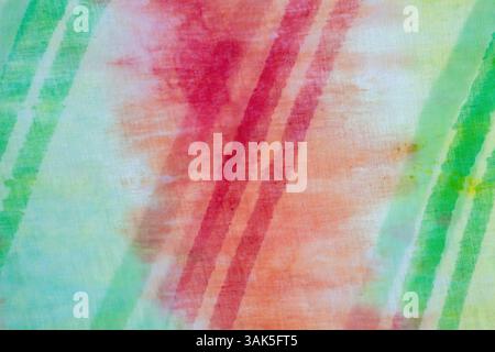 Sfondo astratto con motivo tie-dye rosso, arancione e verde. Questo colorato tie-dye presenta una linea a righe su un tessuto di cotone che crea uno stile astratto Foto Stock
