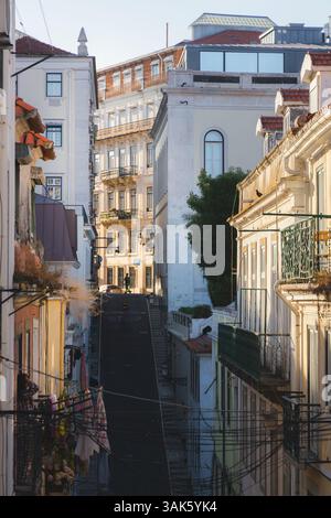 Una strada ripida e tranquilla a Bairro alto, Lisbona, è adornata da lavanderia appesa su edifici storici, che catturano la vita quotidiana tradizionale e il carretto Foto Stock