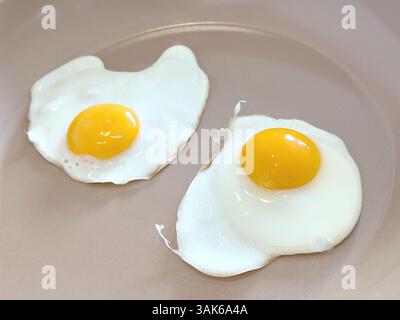 Uova fresche fritte su una padella di ceramica Foto Stock