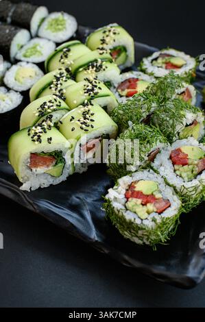 Un set di sushi splendidamente organizzato con coloratissimi rotoli vegani realizzati con verdure fresche, serviti su uno sfondo scuro per un look moderno ed elegante. Foto Stock