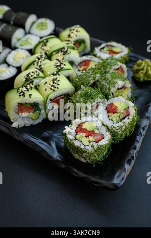 Un set di sushi splendidamente organizzato con coloratissimi rotoli vegani realizzati con verdure fresche, serviti su uno sfondo scuro per un look moderno ed elegante. Foto Stock