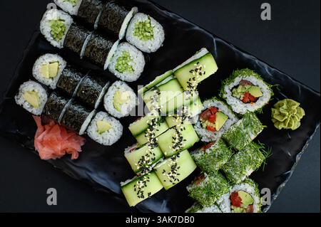 Un set di sushi splendidamente organizzato con coloratissimi rotoli vegani realizzati con verdure fresche, serviti su uno sfondo scuro per un look moderno ed elegante. Foto Stock