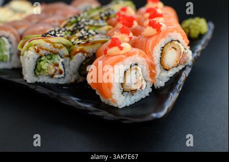 Un variopinto assortimento di sushi con panini con avocado, salmone e tonno, presentati in uno stile pulito e moderno. Foto Stock