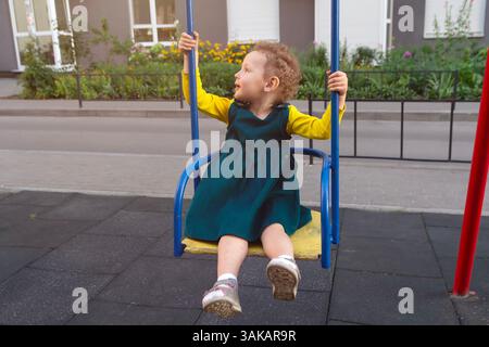 Una ragazza riccia in abito cavalca su un'altalena. Persone Foto Stock