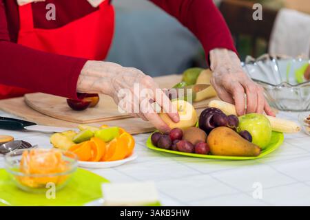 Primo piano di una donna anziana che taglia frutta in cucina a casa. Foto Stock