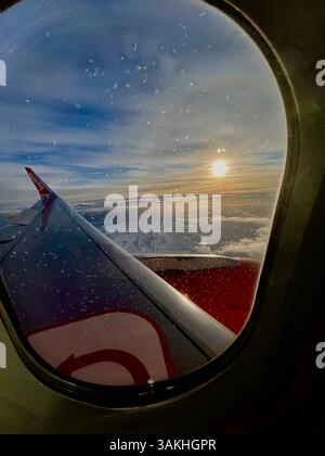 Il sole tramonta all'orizzonte visto da una finestra dell'aereo che si avvicina all'Islanda con nuvole e cielo blu Foto Stock